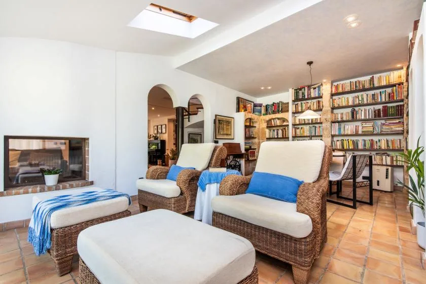 Una sala luminosa con asientos de mimbre, una chimenea y estanterías.