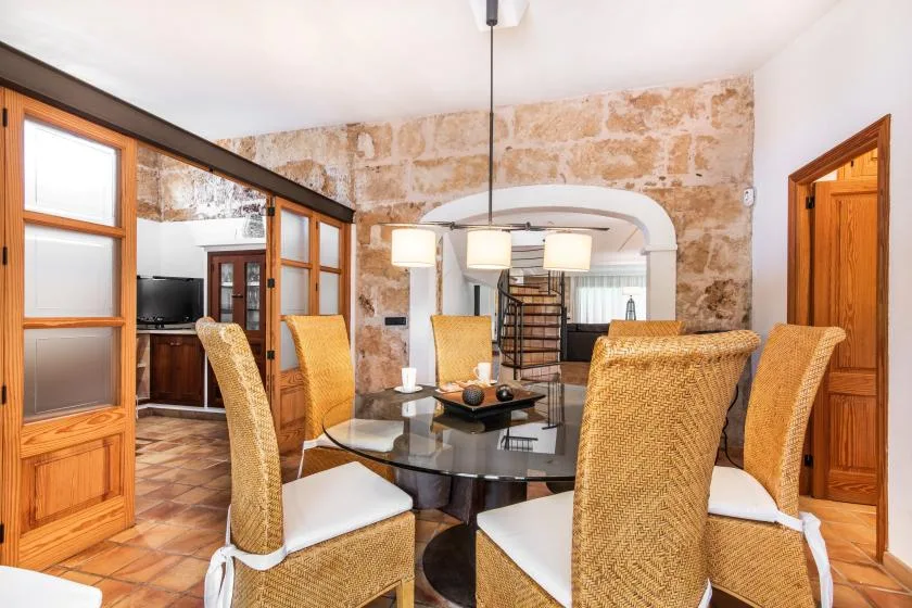 Comedor con asientos de mimbre alrededor de una mesa de cristal y lámparas colgantes.