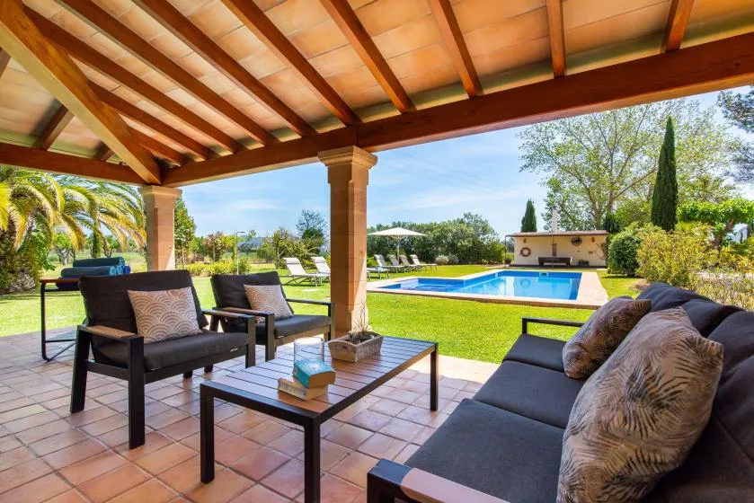 Un patio cubierto con asientos exteriores da a una piscina y un jardín.