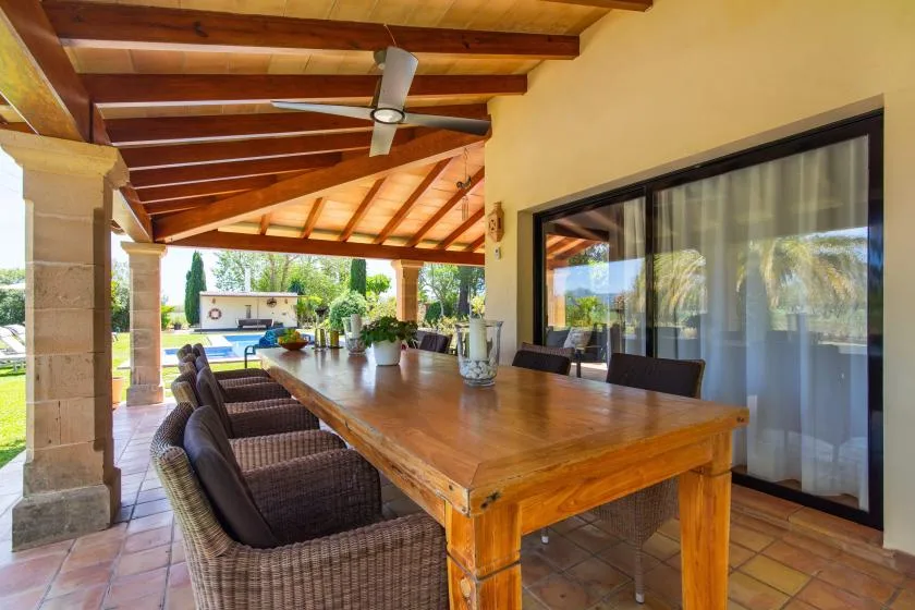 Un patio cubierto con una larga mesa de comedor de madera y asientos acolchados.