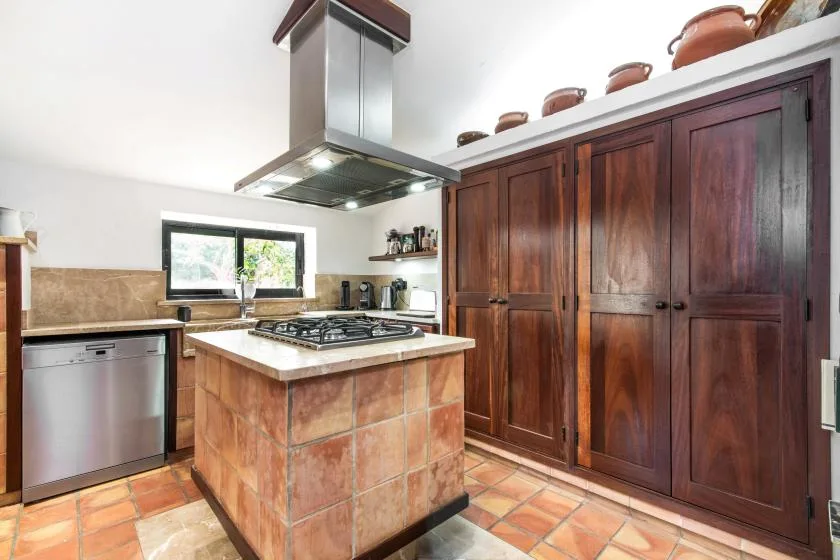 Una cocina con una isla central para cocinar, gabinetes de madera y baldosas de color terracota.