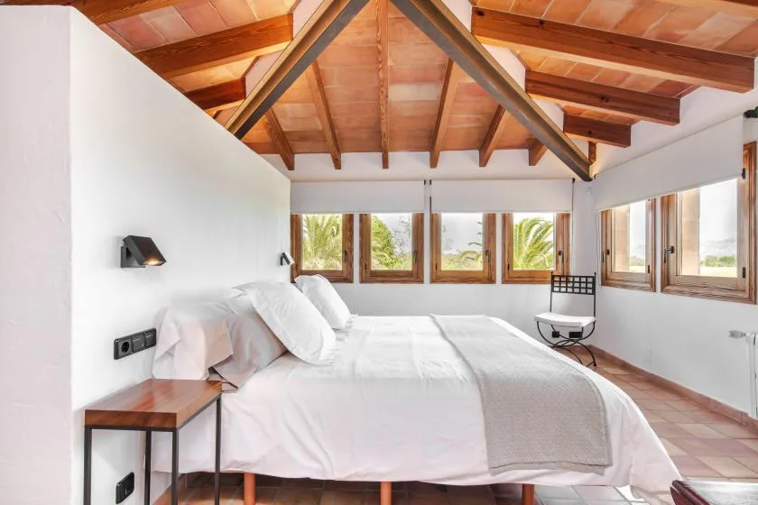 Un dormitorio con una cama grande bajo un techo inclinado de madera y ventanas.