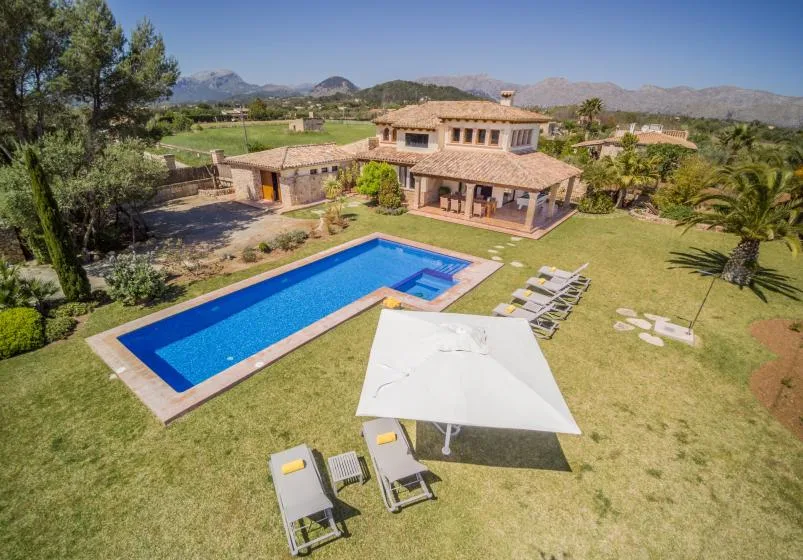 Una casa y una piscina están en un jardín cuidado con vistas a las montañas.