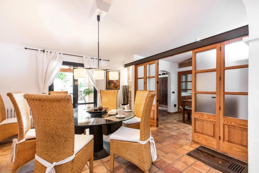 Comedor con asientos tejidos alrededor de una mesa, junto a puertas de vidrio con marcos de madera.