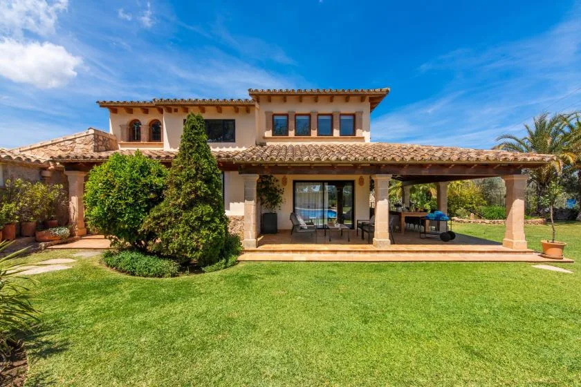 Una casa de dos plantas con patio cubierto da a un césped verde.
