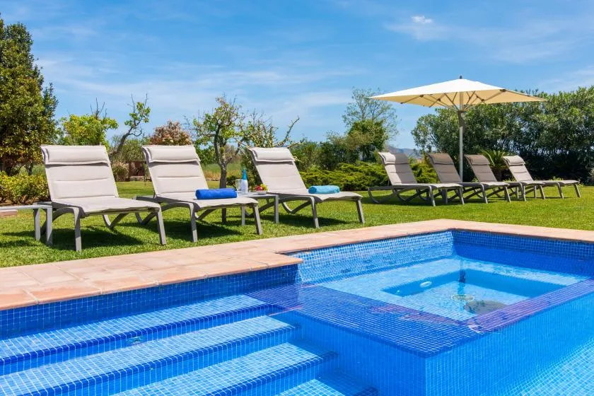 Una piscina al aire libre con tumbonas y una sombrilla grande sobre el césped.