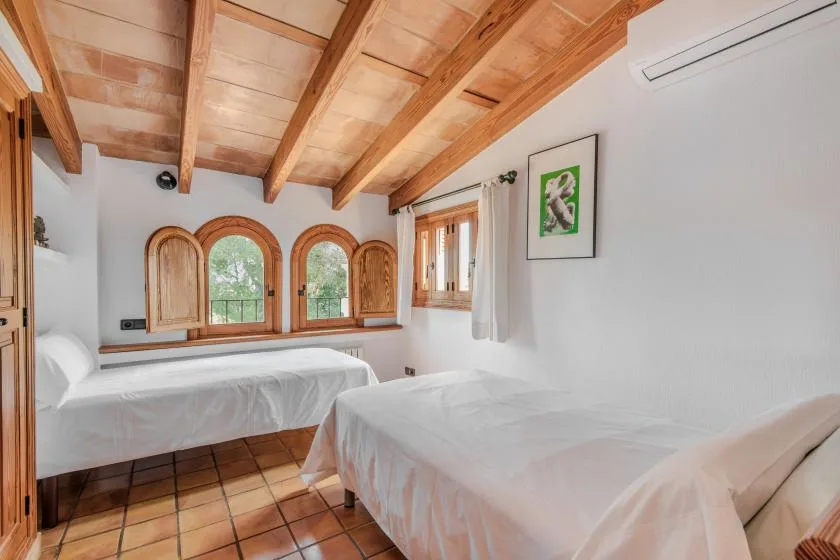Un dormitorio luminoso con dos camas, ventanas arqueadas y vigas de madera a la vista.