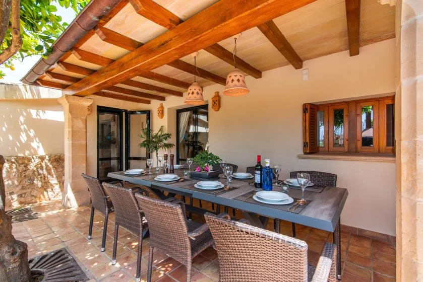 Comedor exterior cubierto con una mesa larga y asientos de mimbre.