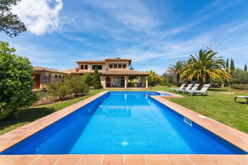 Una piscina exterior está frente a una casa, con tumbonas sobre el césped.