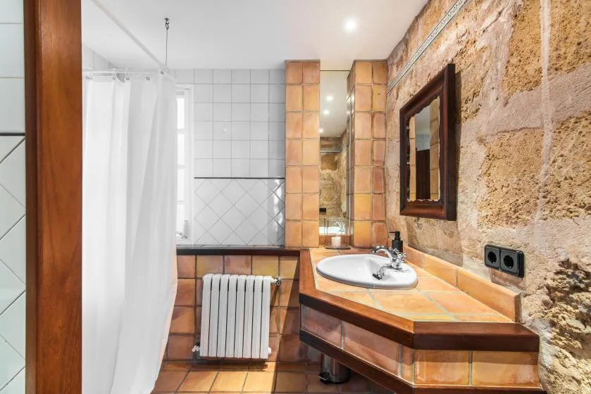 Un baño revestido de azulejos con lavabo, espejo y cortina de ducha blanca.