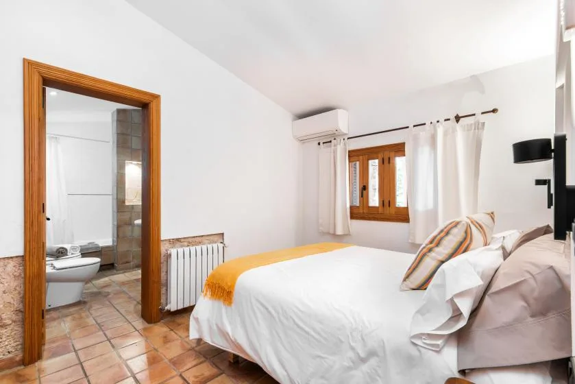 Un dormitorio con una cama, una ventana con cortinas y un baño contiguo.