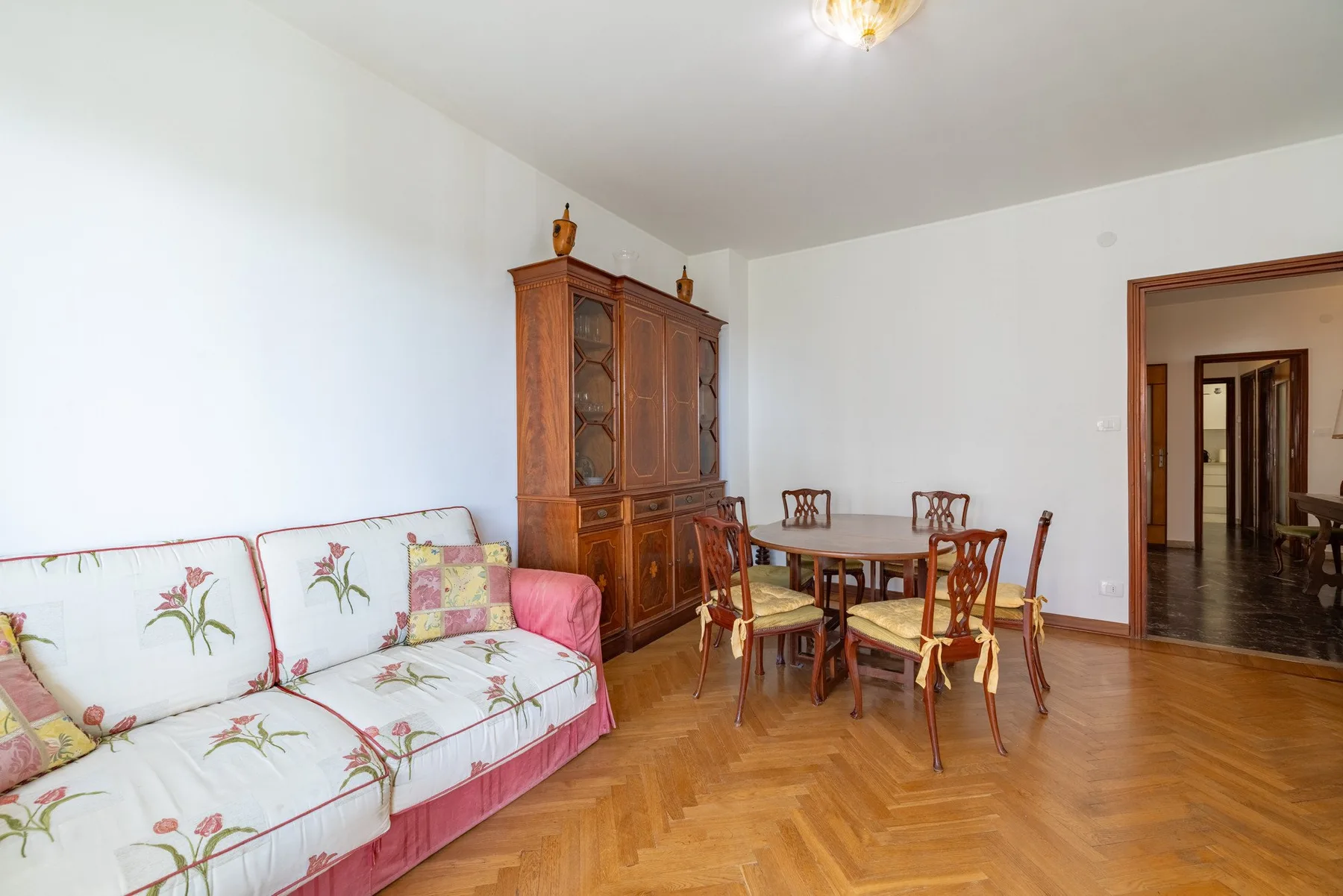 A dining and sitting room with a floral sofa and wooden dining furniture.