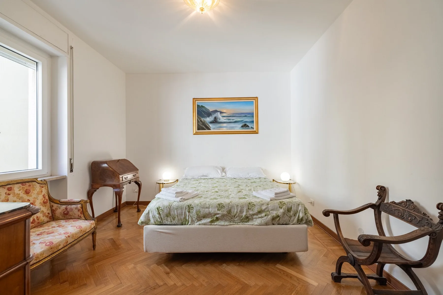 A bedroom with a bed, bedside tables, and wooden seating.
