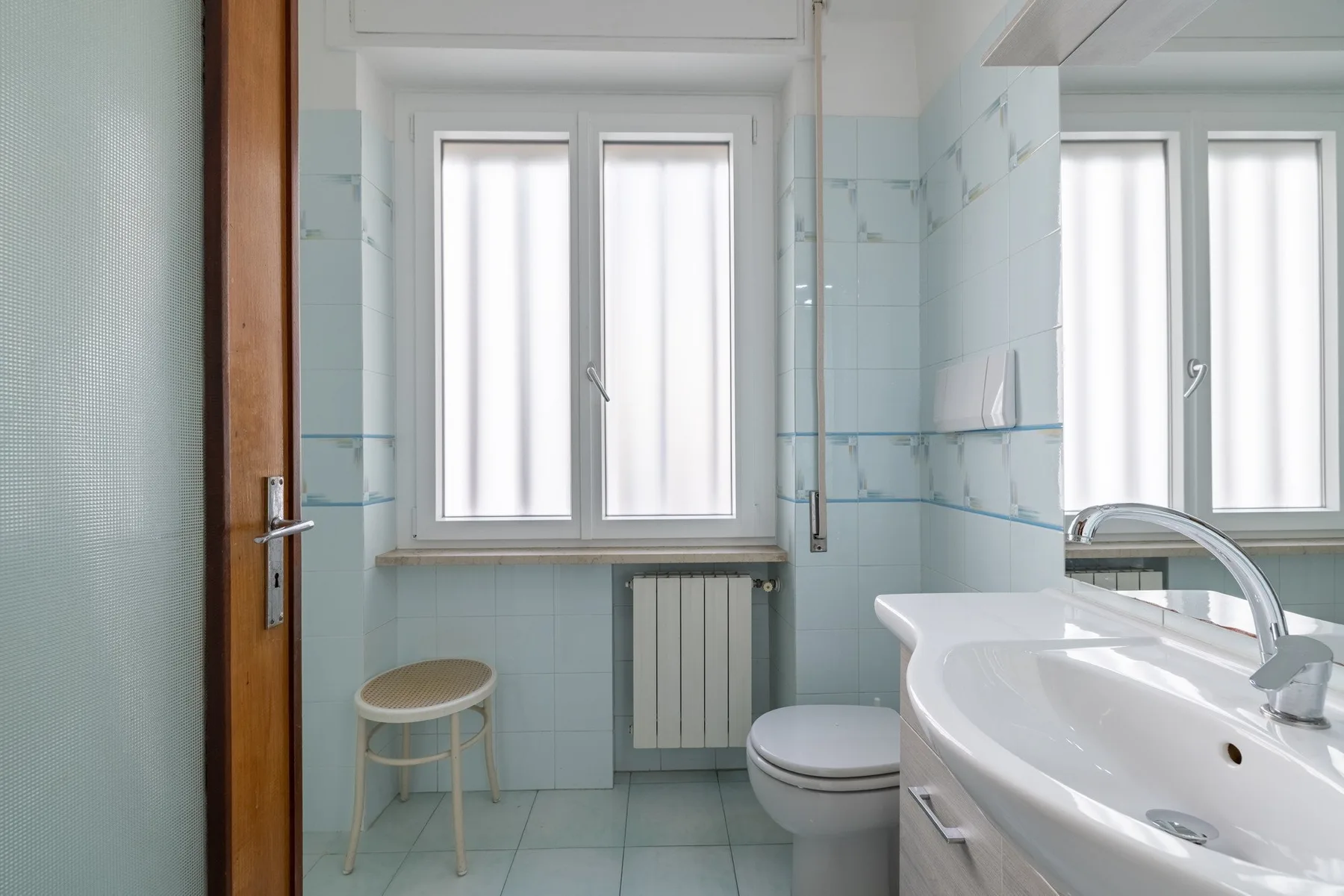 A tiled bathroom with a sink, toilet, and frosted windows.