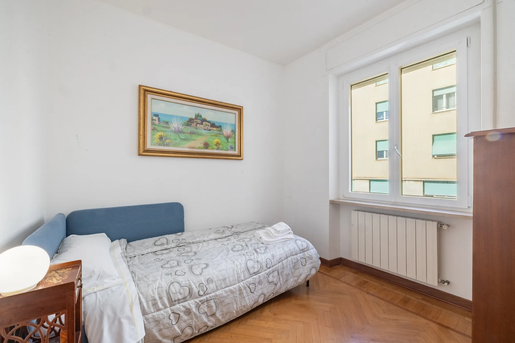A bedroom with a bed, framed artwork, and a window overlooking a neighboring building.