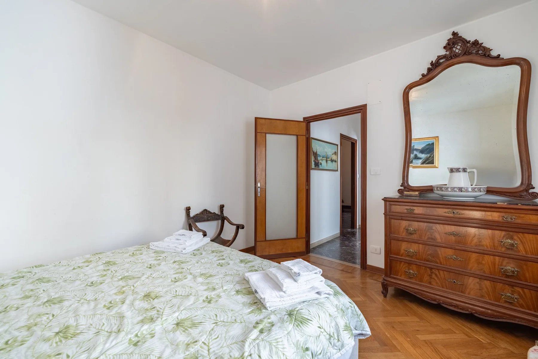 A bedroom with a bed, folded linens, and a wooden dresser topped by a mirror.