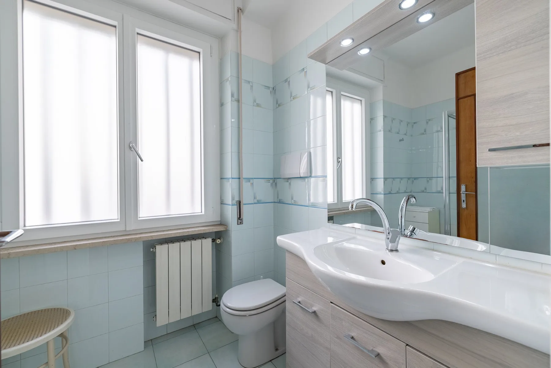 A bright bathroom with a large sink, toilet, and windows.