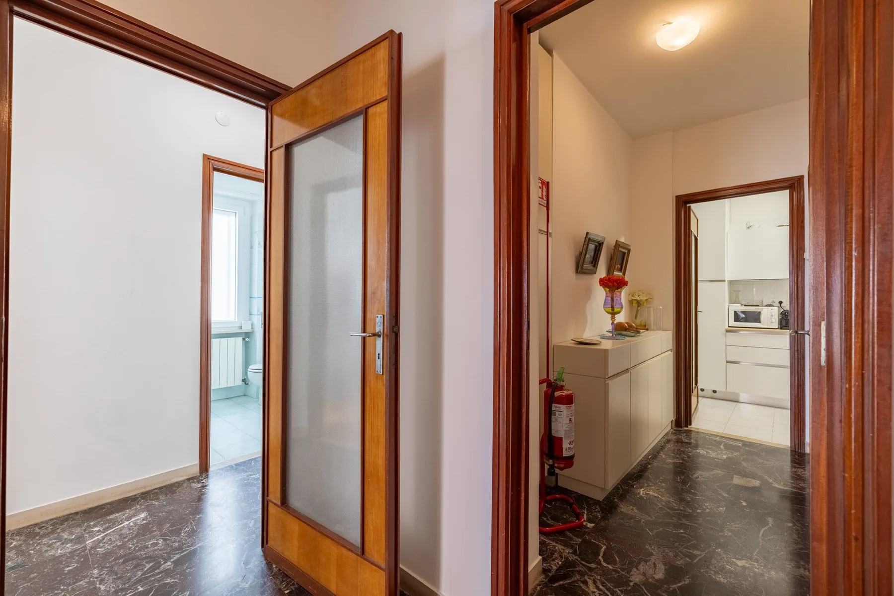 An interior hallway with wooden doorways, a cabinet, and dark flooring.