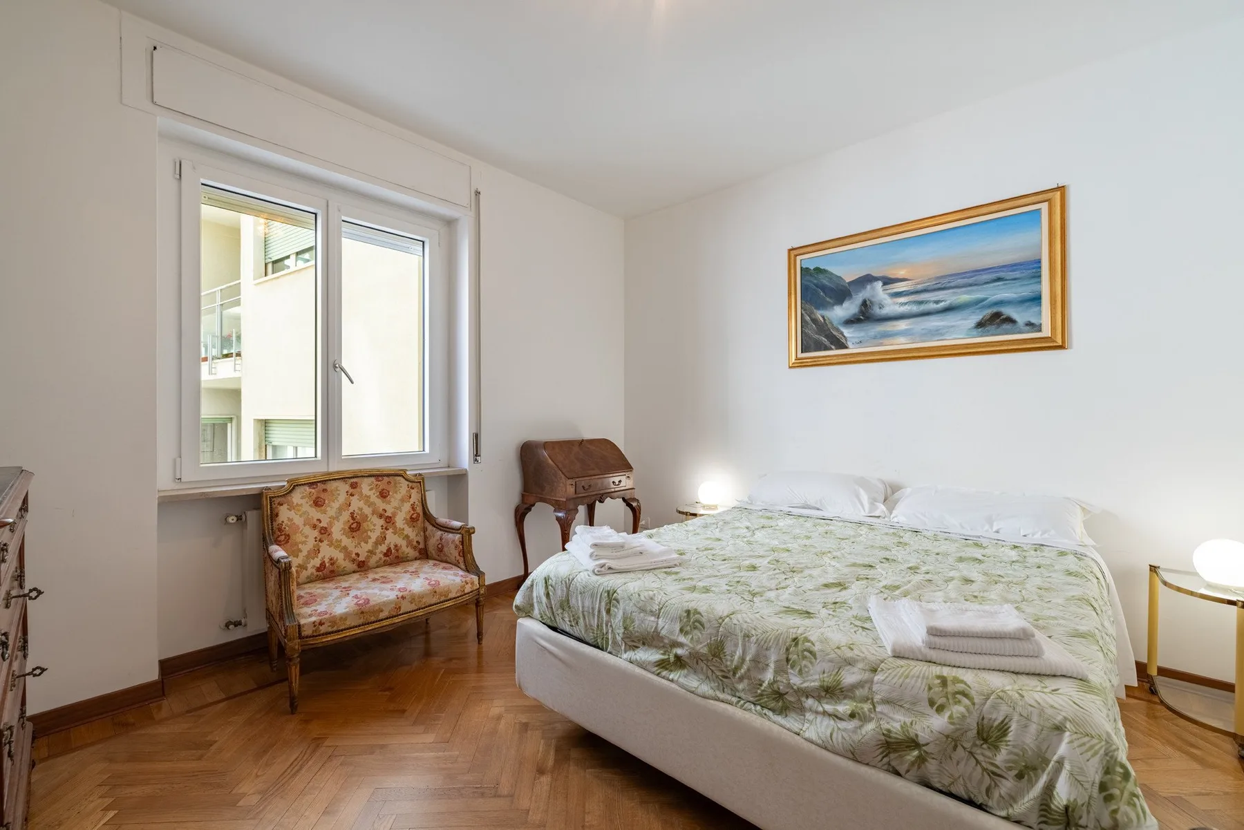 Un dormitorio con una cama, una ventana y un cuadro de paisaje marino.