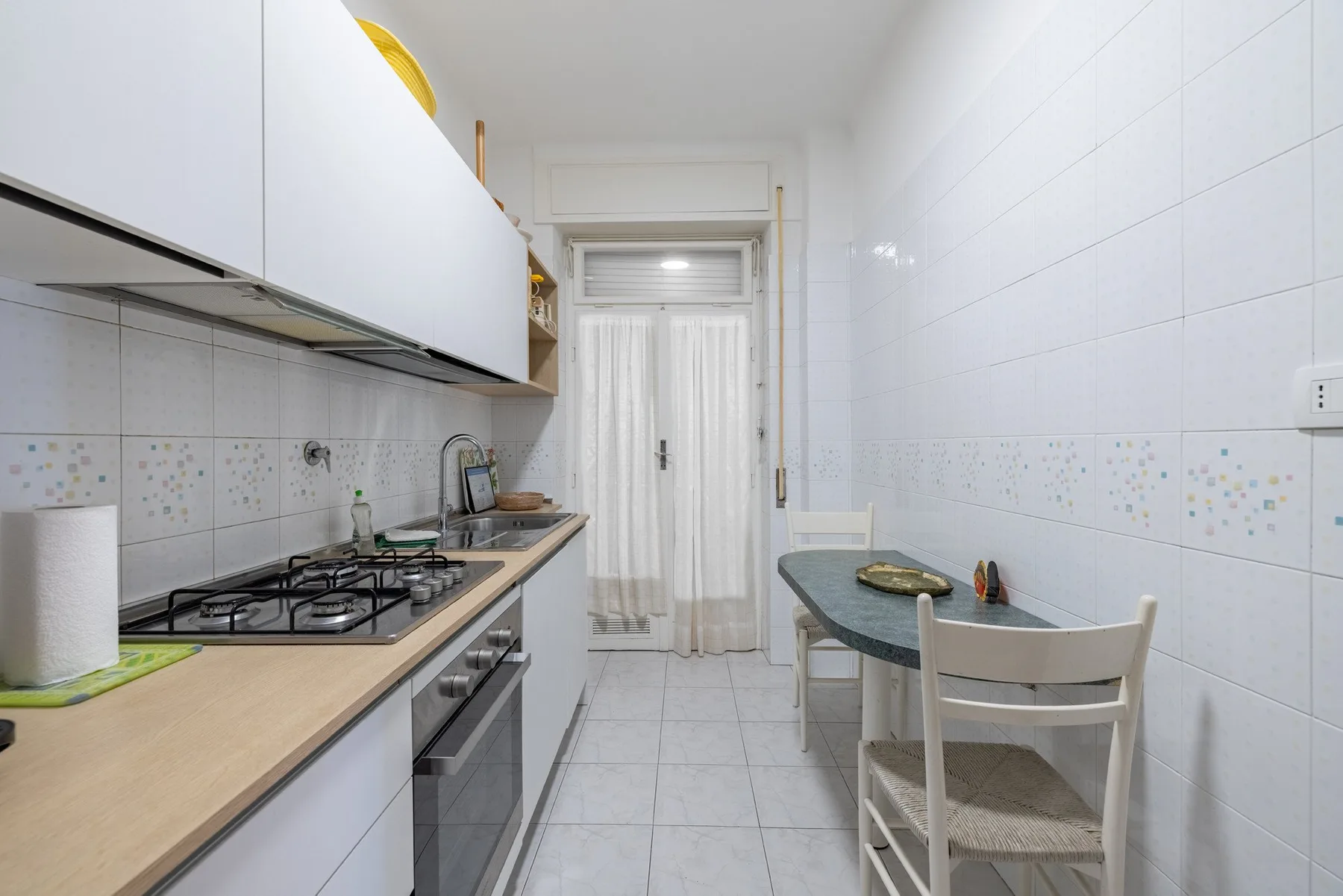 A narrow kitchen with a countertop, stovetop, and small dining table.