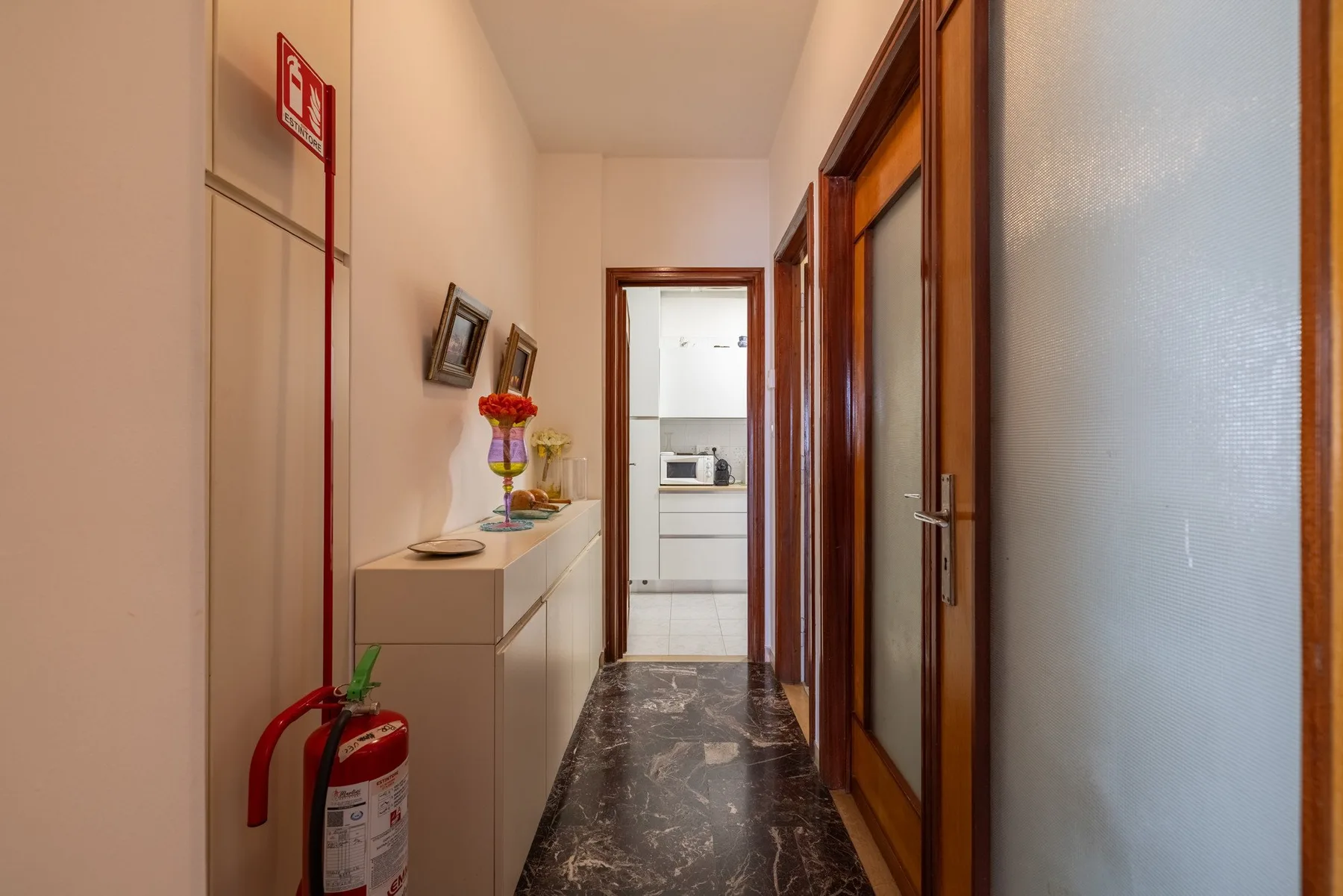 A hallway with a marble-patterned floor and a doorway opening into a kitchen.