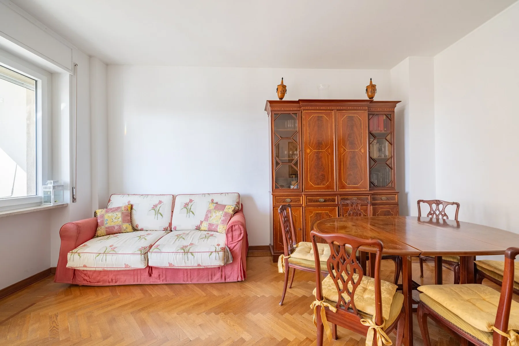 Una luminosa sala de estar y comedor con un sofá floral y una mesa de comedor de madera.