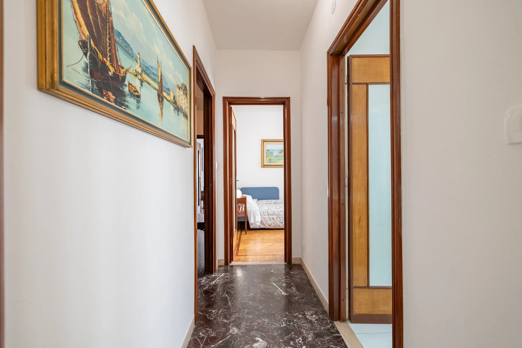 A narrow hallway with framed artwork leads to a bedroom.