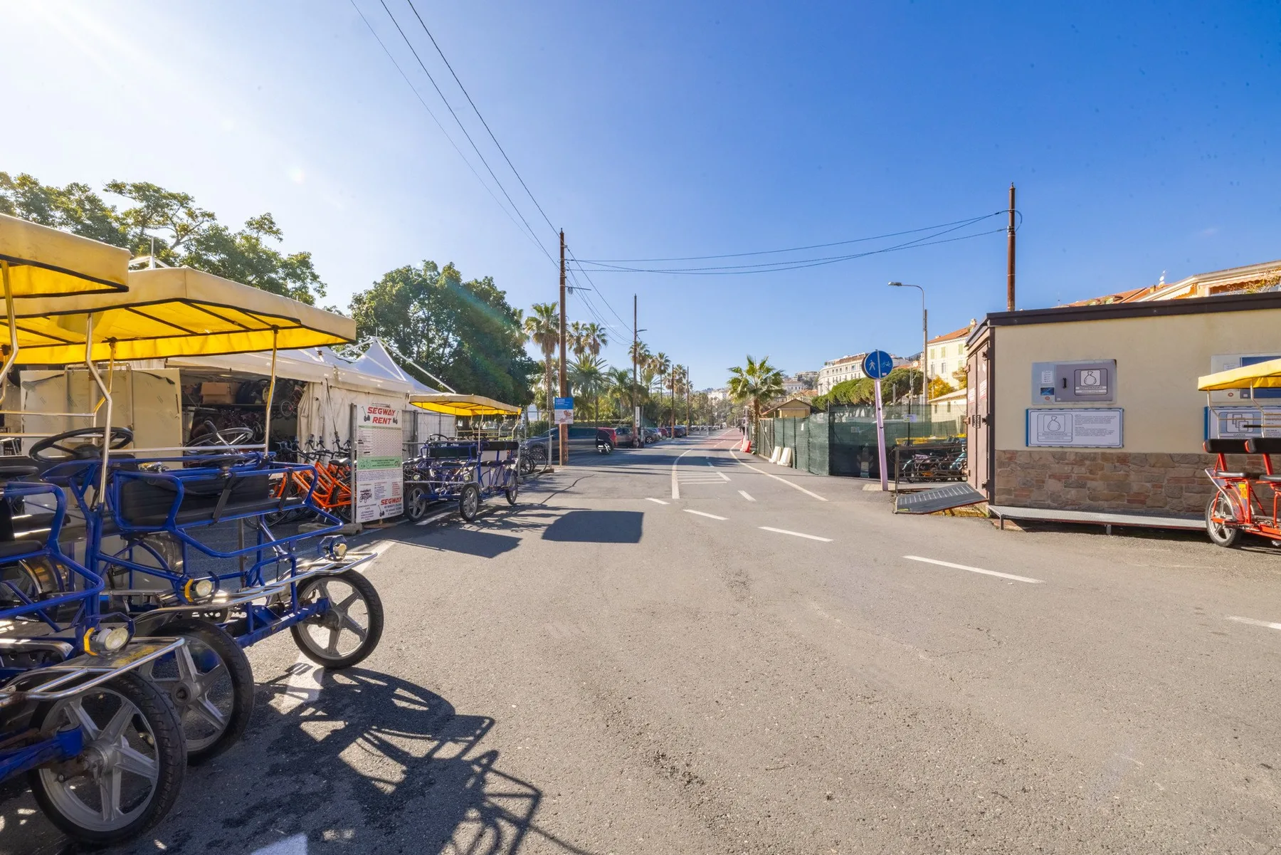 A sunny outdoor street scene with parked bicycles beside low buildings.