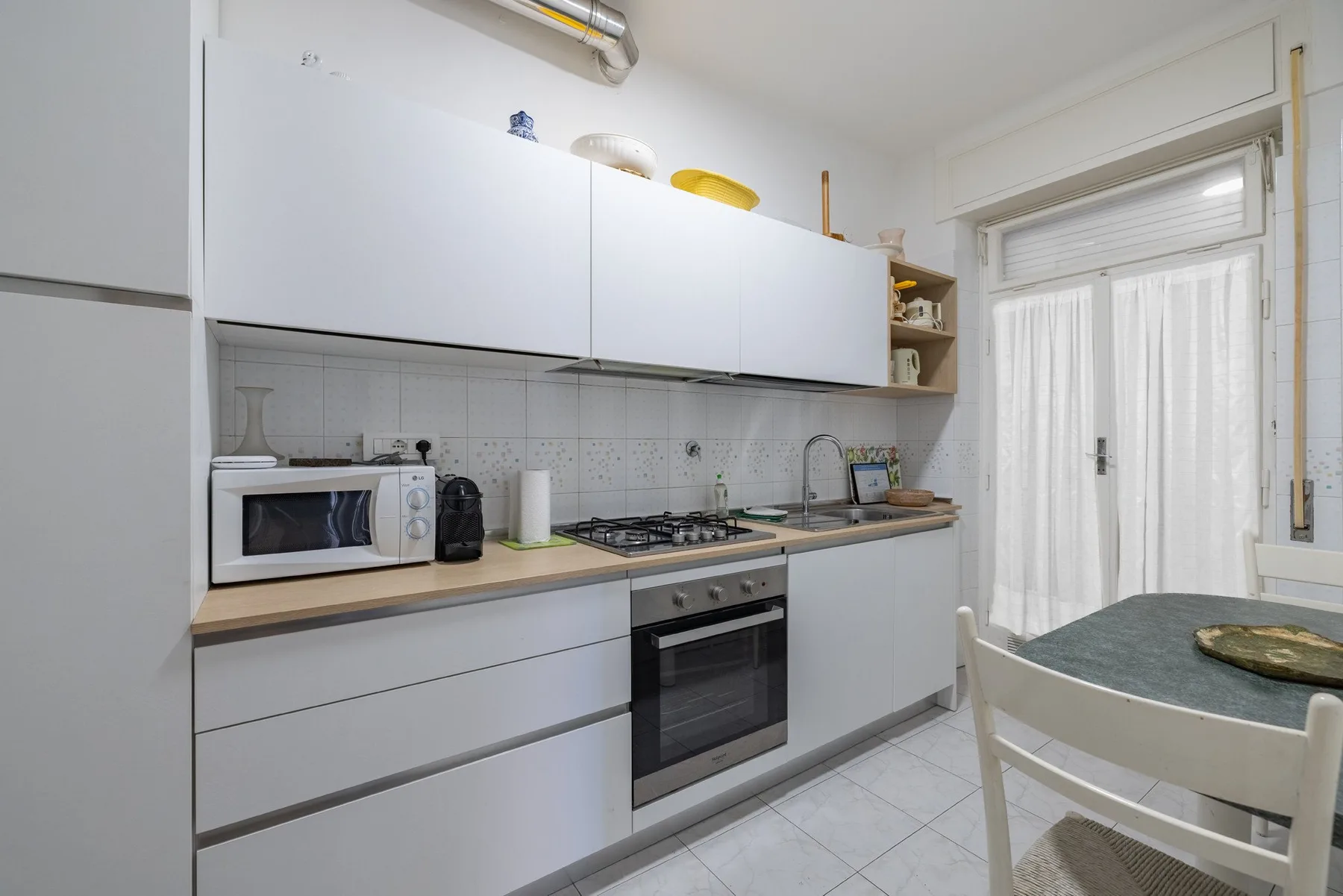 Una cocina compacta con armarios blancos, una placa de cocina y una mesa de comedor.