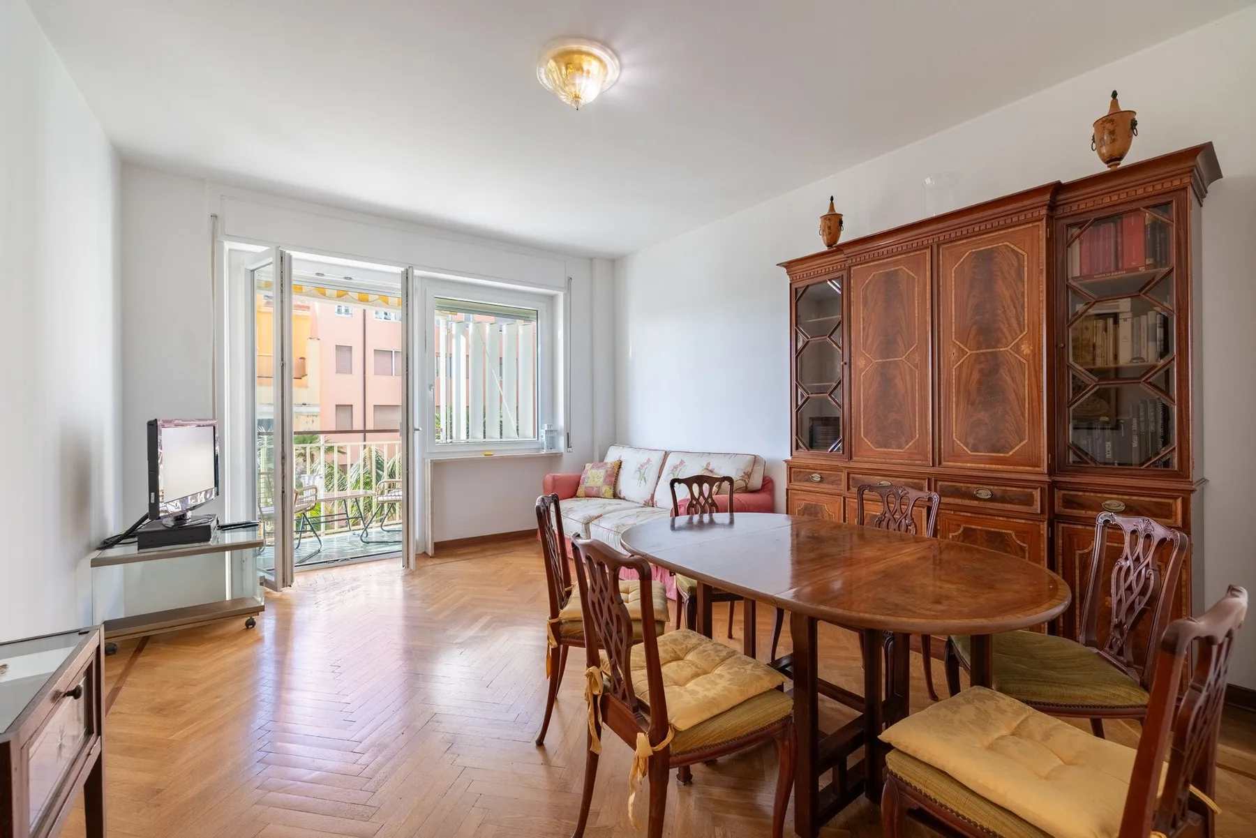 A dining and living area with a wooden table and seating beside a balcony window.