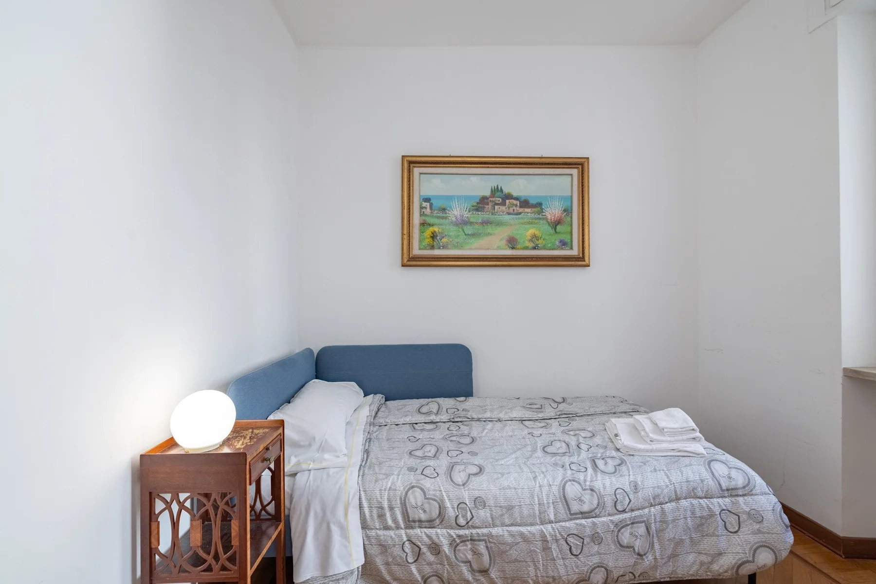 A bedroom with a bed, patterned bedding, and a framed picture on the wall.