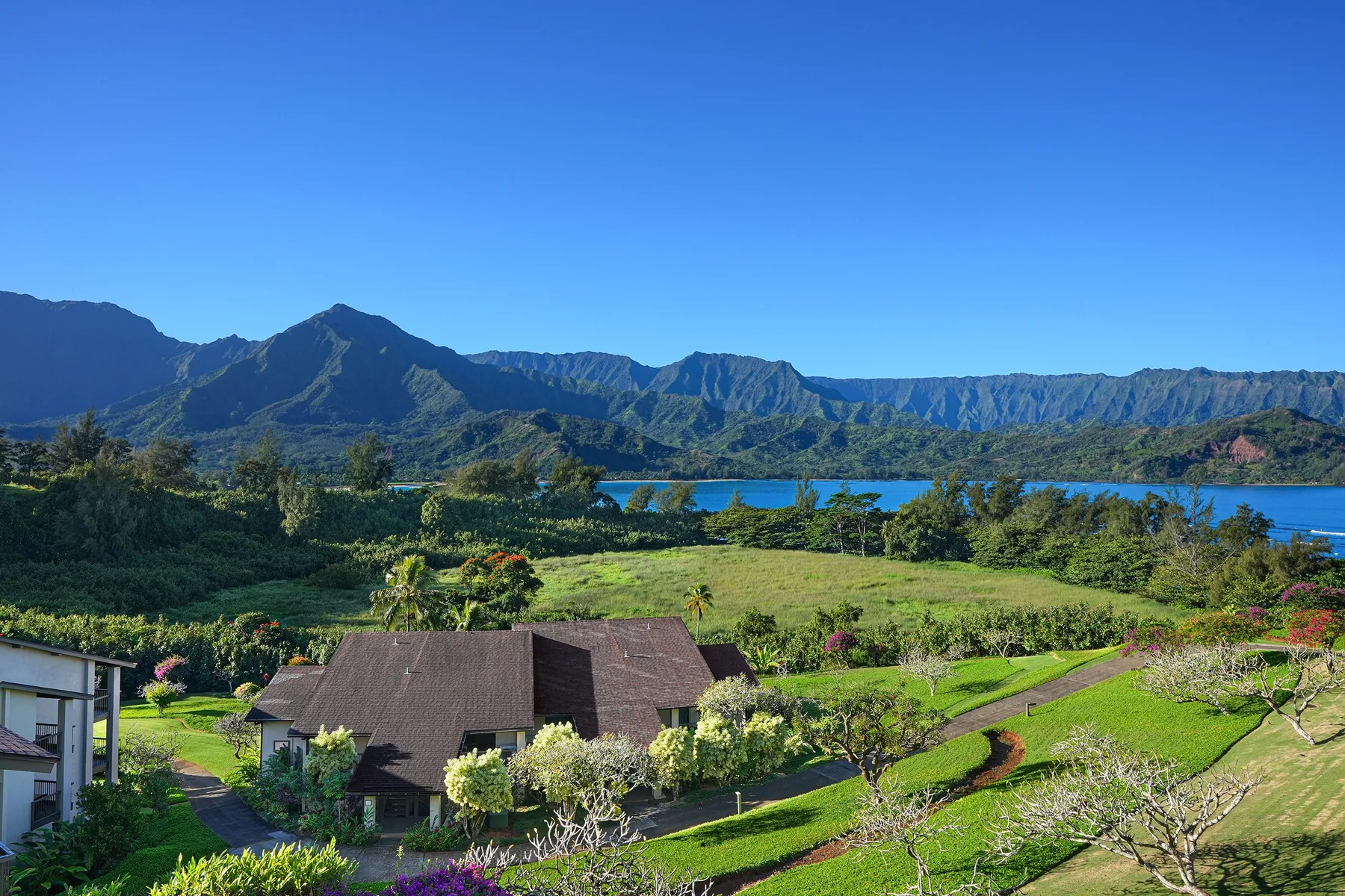 A landscaped garden and low buildings overlook a lake and mountain range.