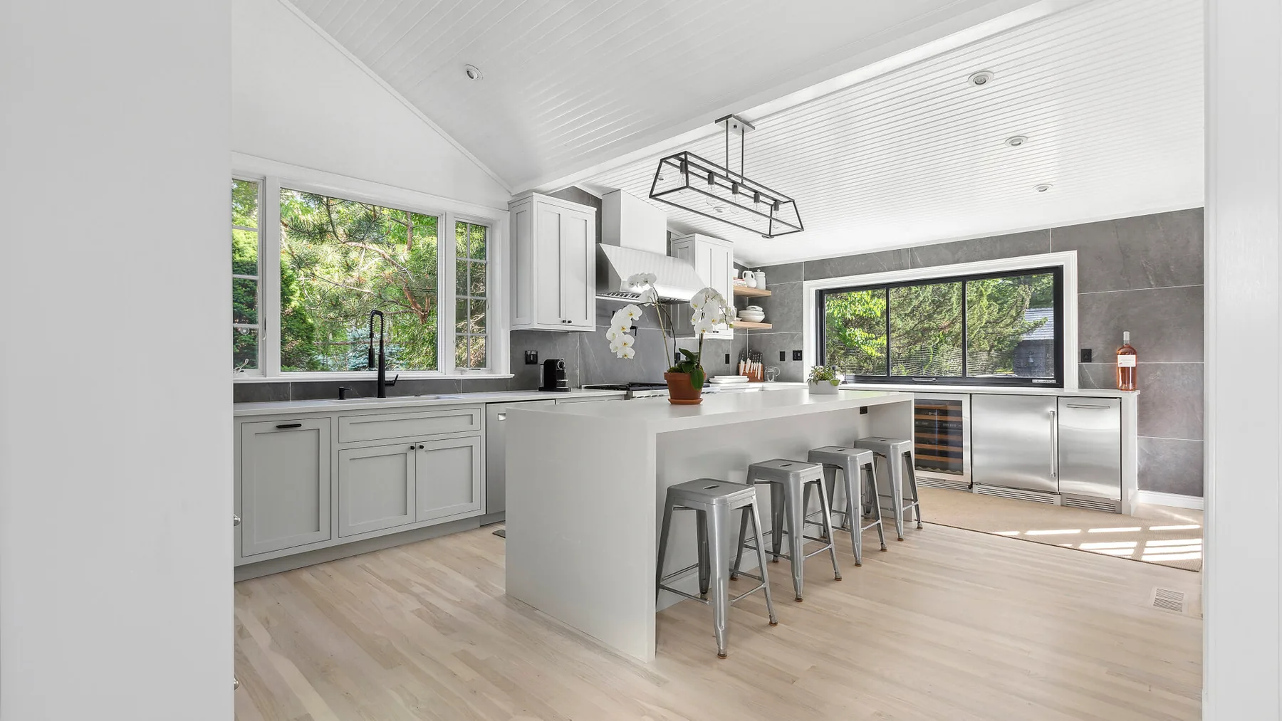 Una cocina luminosa con gabinetes blancos, una isla central y ventanas grandes.