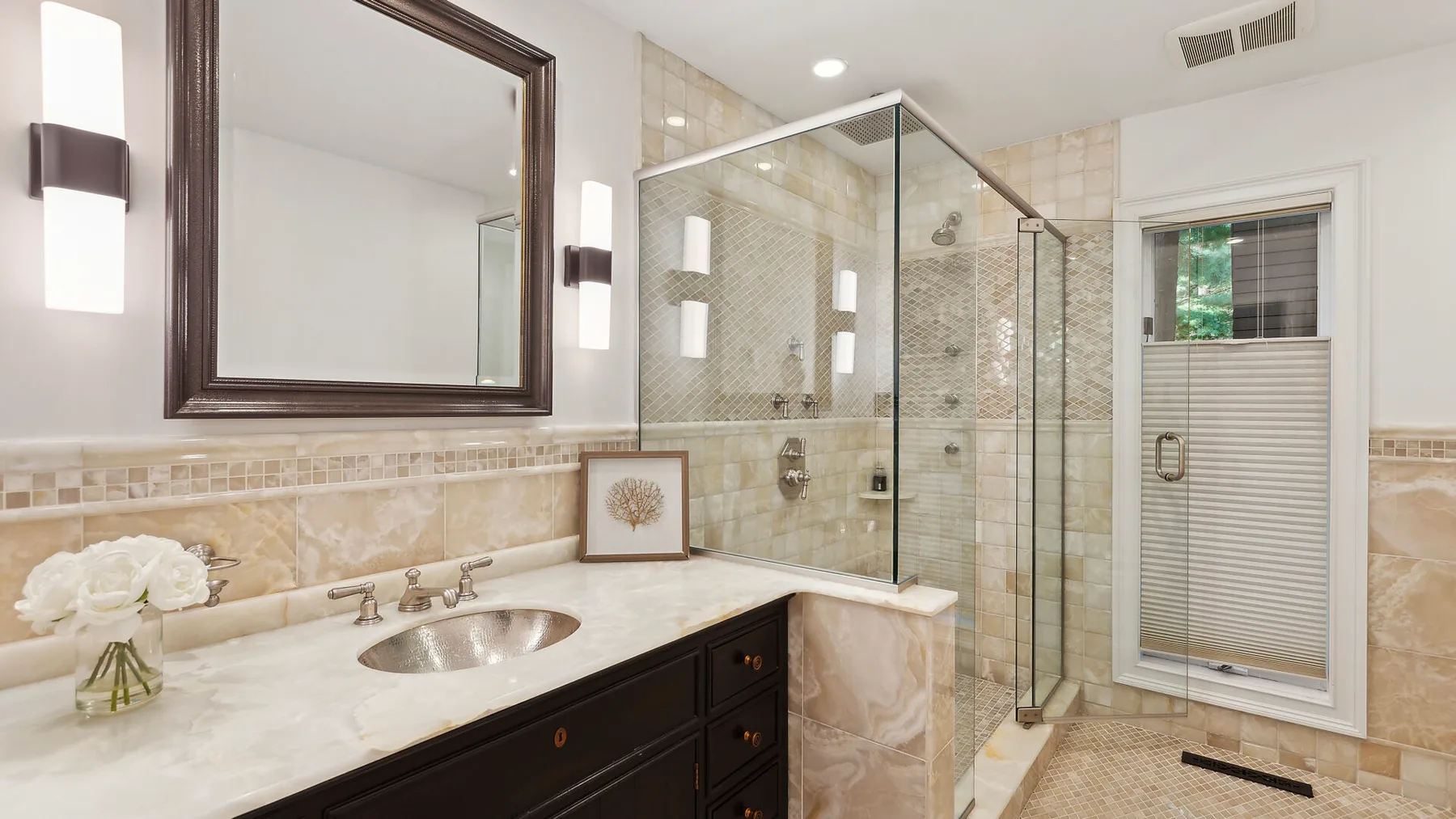 Un baño con azulejos, una ducha de vidrio, tocador y ventana.