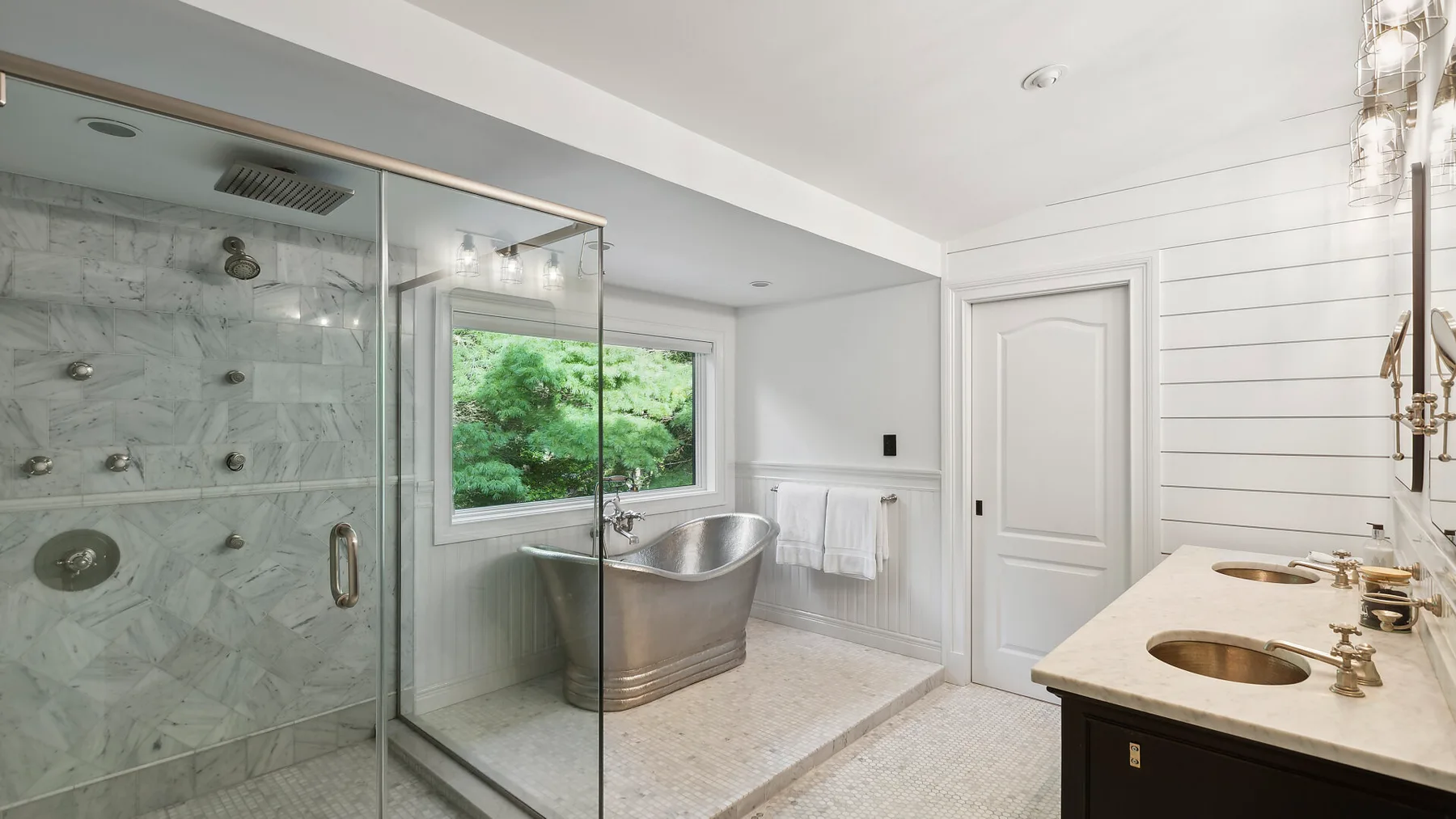 Un baño luminoso cuenta con una ducha de vidrio, una bañera y un tocador con dos lavabos.