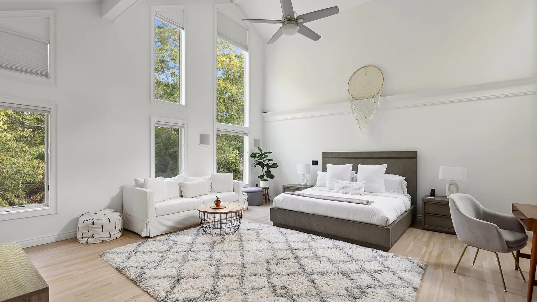 Un dormitorio luminoso con una cama grande, una zona de estar y ventanas altas.