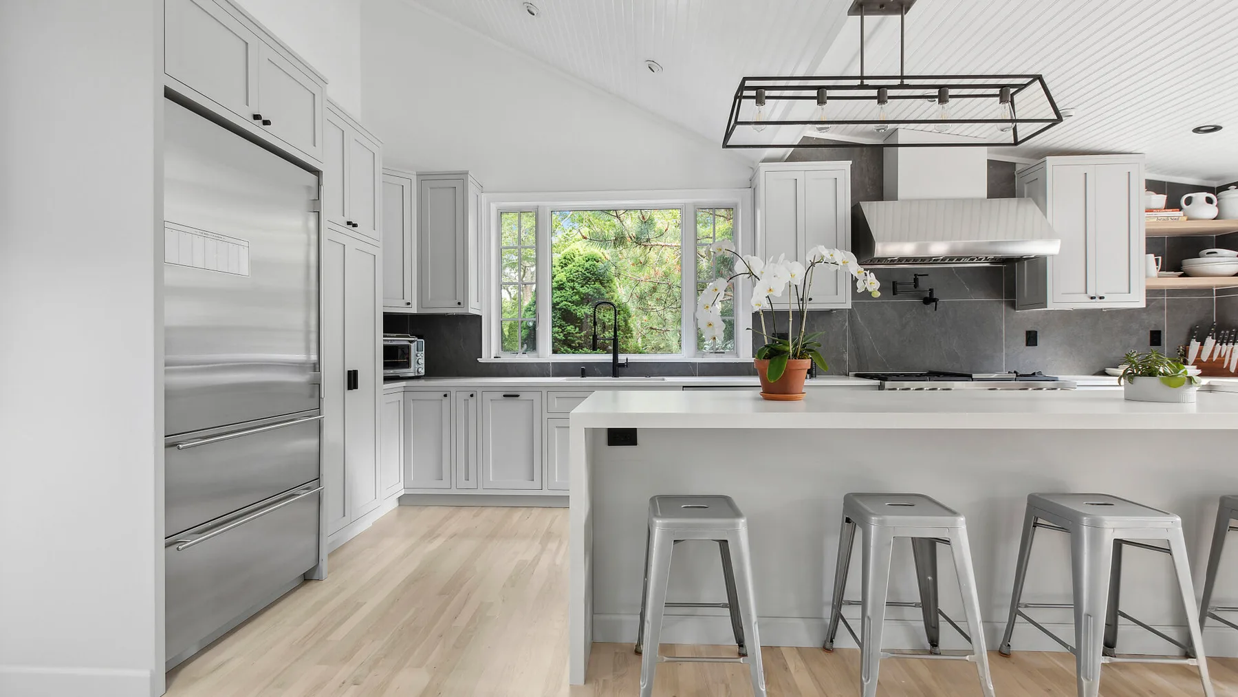 Una cocina luminosa con una isla grande, asientos y una ventana con vistas a la vegetación.