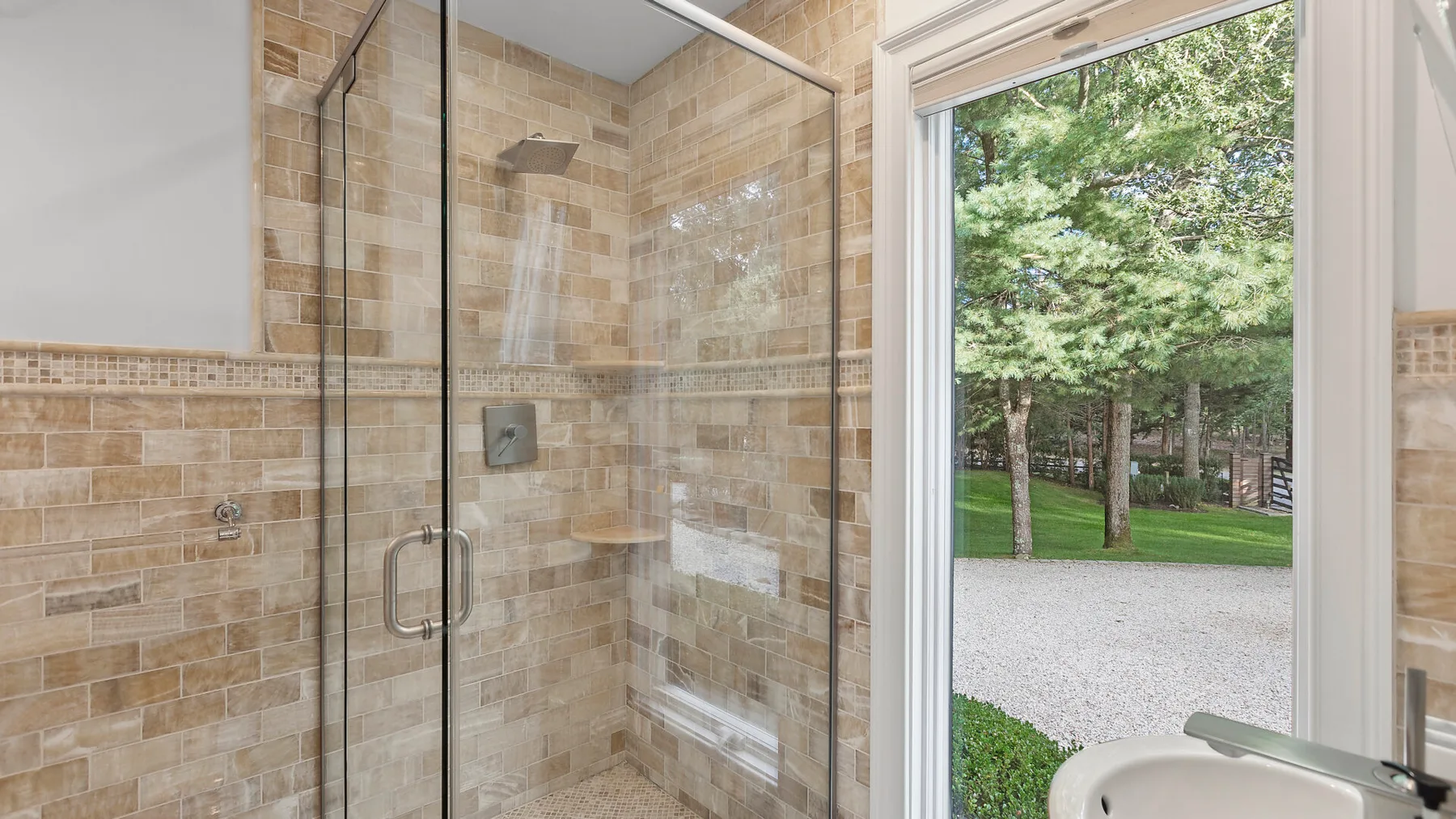 Un baño revestido de azulejos, con ducha de vidrio y una ventana con vistas a la vegetación.