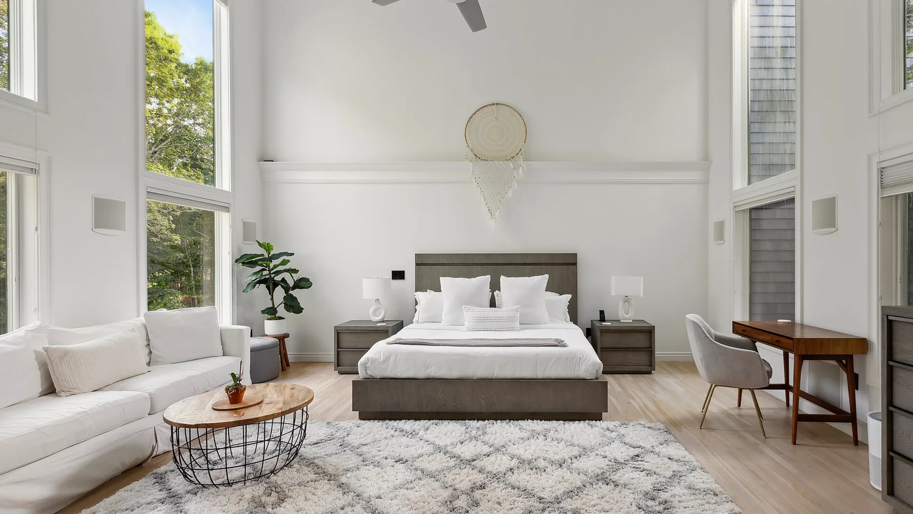 Un dormitorio luminoso con una cama, asientos y ventanas altas.