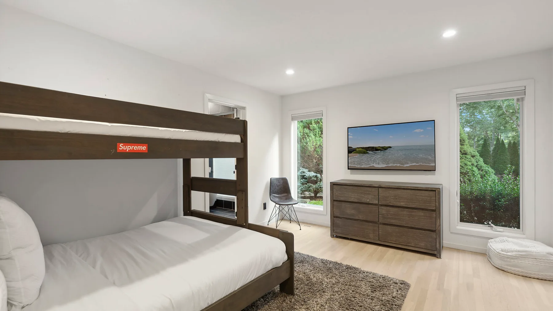 Un dormitorio luminoso con una litera, una cómoda y un televisor en la pared.
