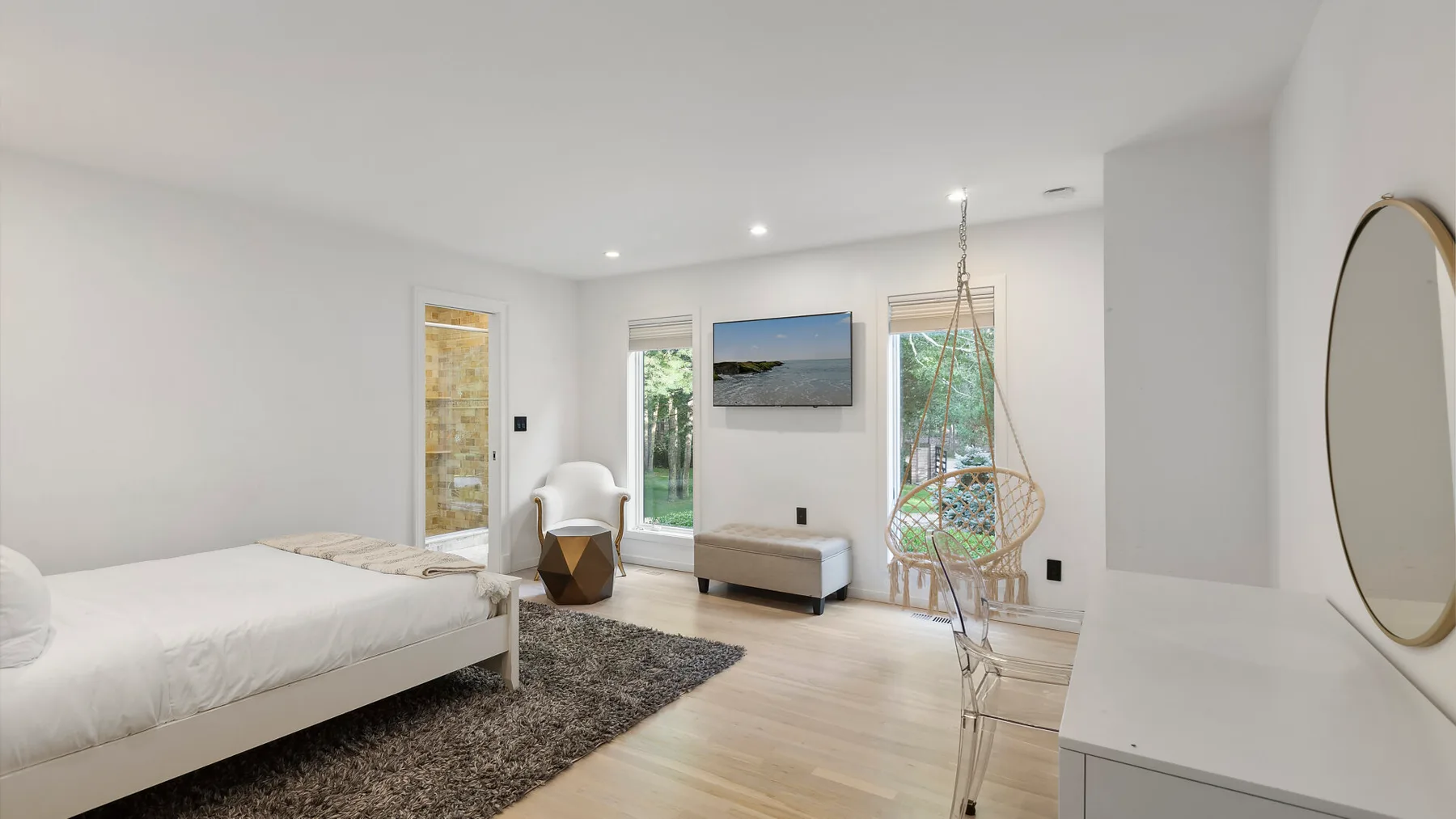 Un dormitorio luminoso con una cama, un televisor y una silla colgante.