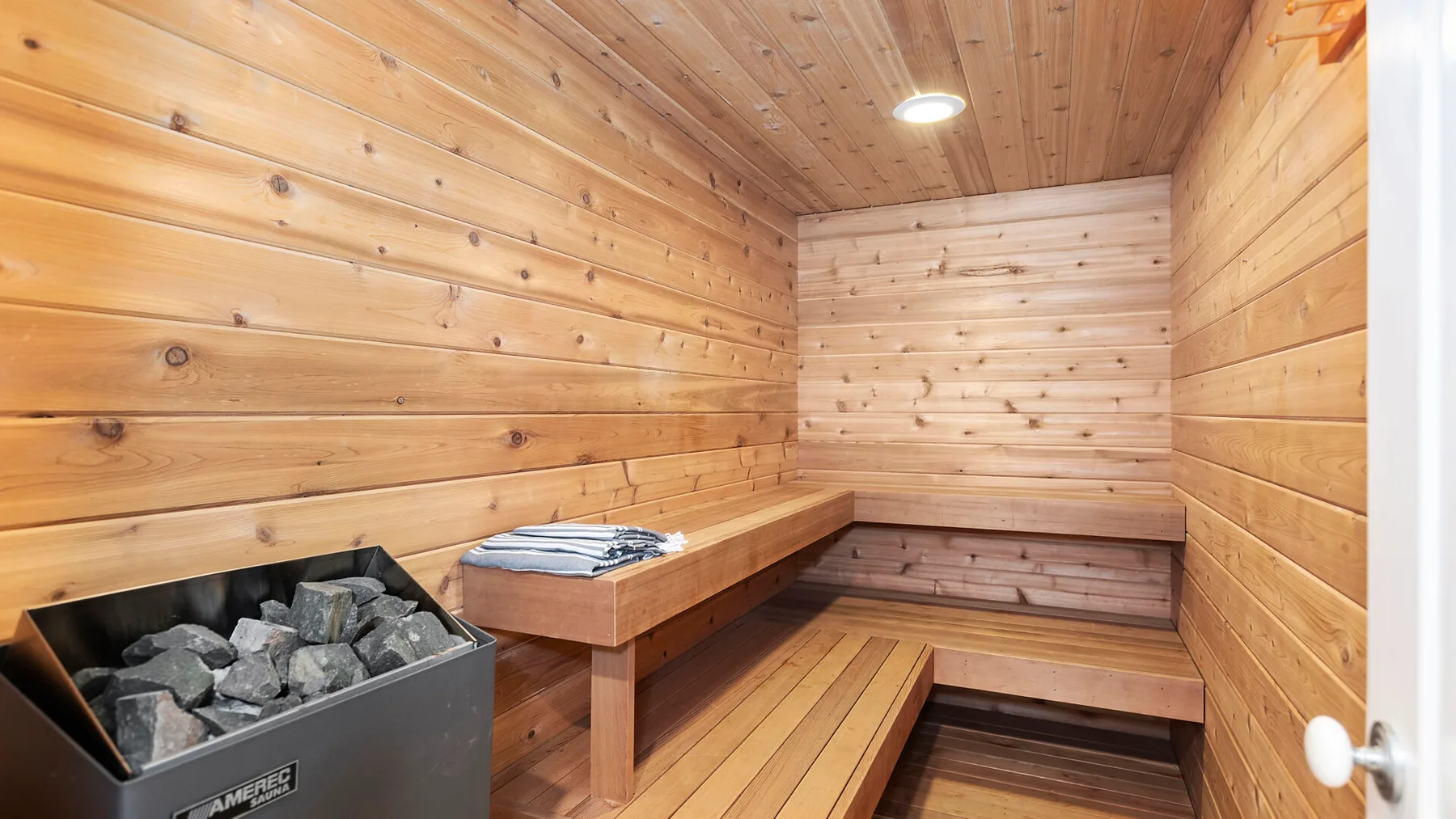 Una sauna revestida de madera con asientos escalonados y un calentador de piedras.