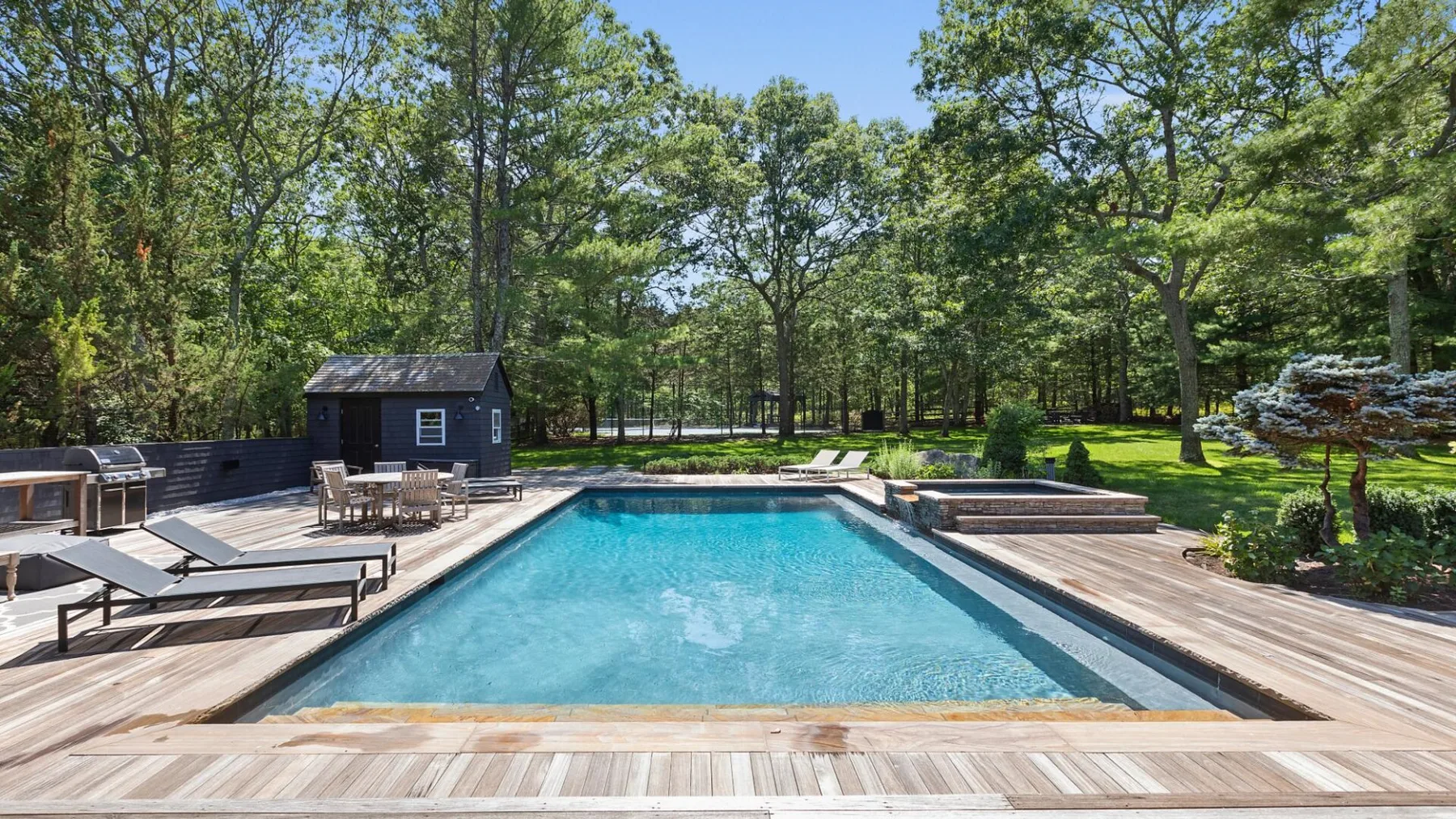 Una piscina al aire libre está rodeada por una terraza de madera y árboles.