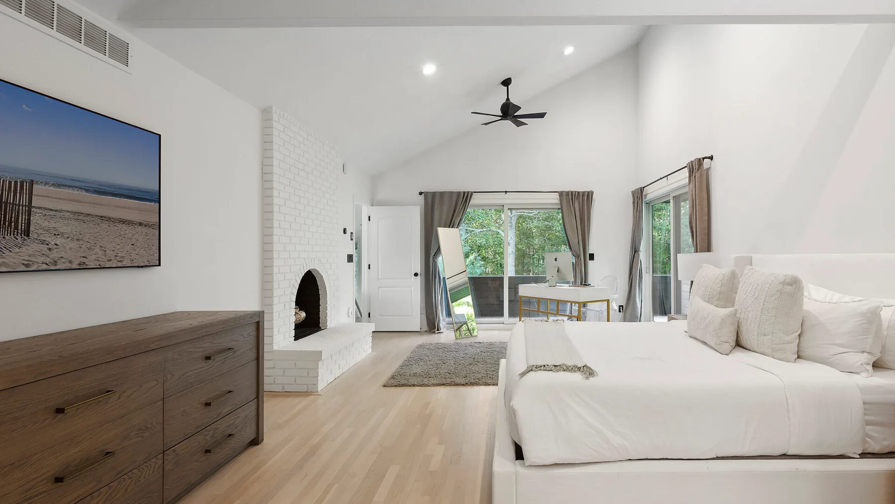 Un dormitorio luminoso con una cama grande y una cómoda bajo una pantalla montada en la pared.