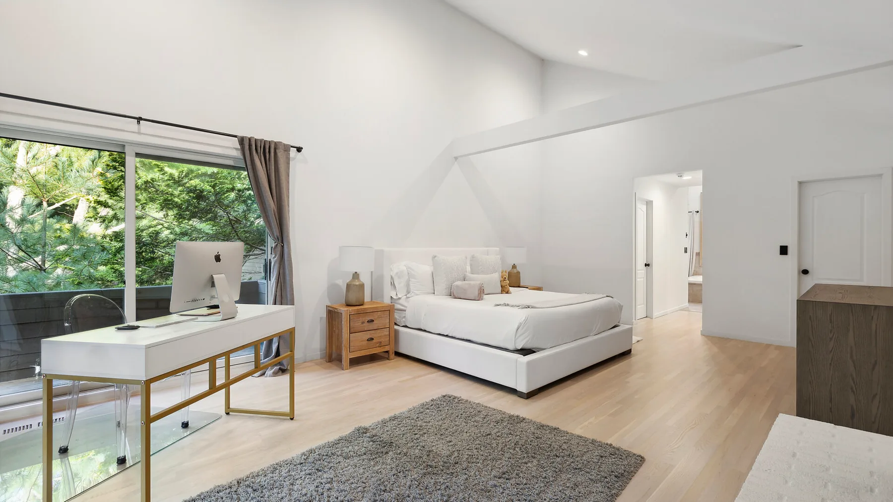 Un dormitorio luminoso con una cama, un escritorio y una gran ventana con vistas a la vegetación.