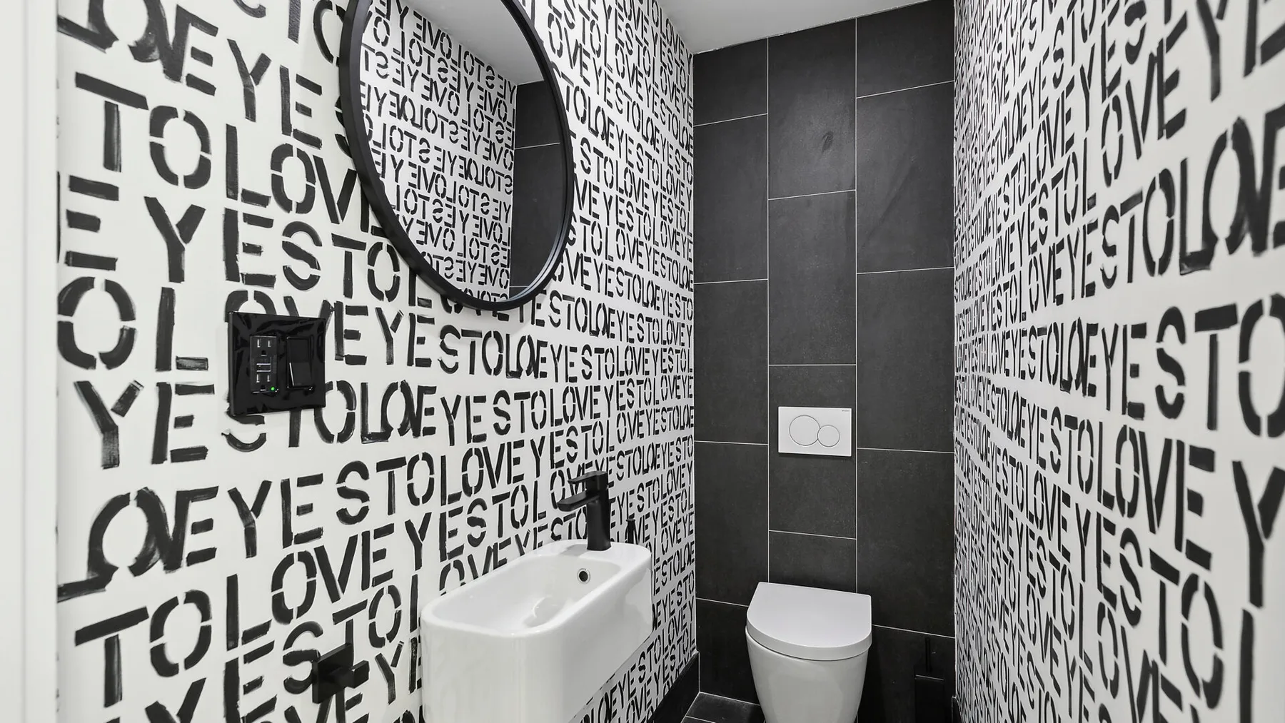 Un baño moderno con letras negras y blancas llamativas en las paredes y azulejos oscuros.