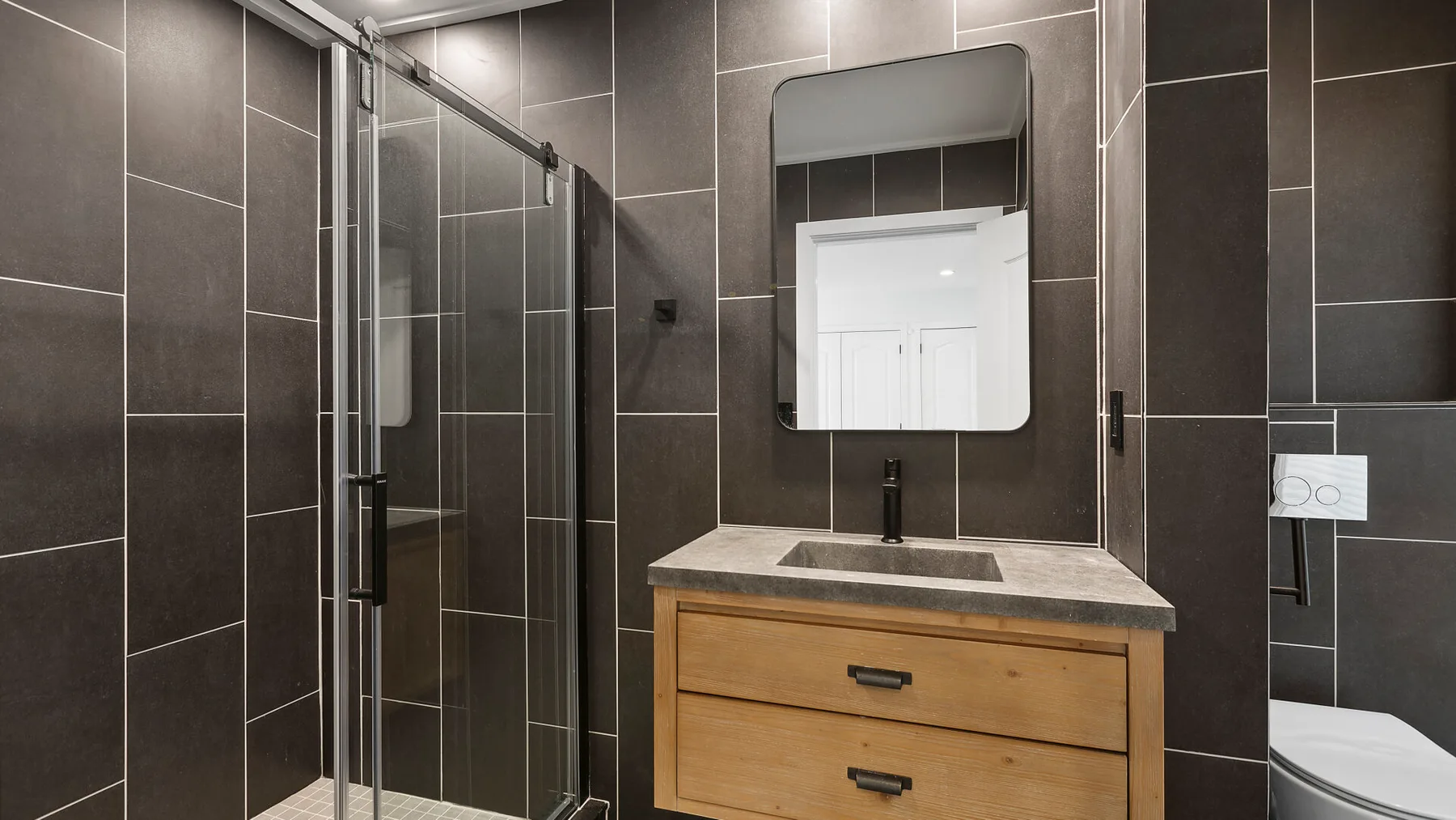 Baño con azulejos, ducha de vidrio, lavabo y mueble de madera.