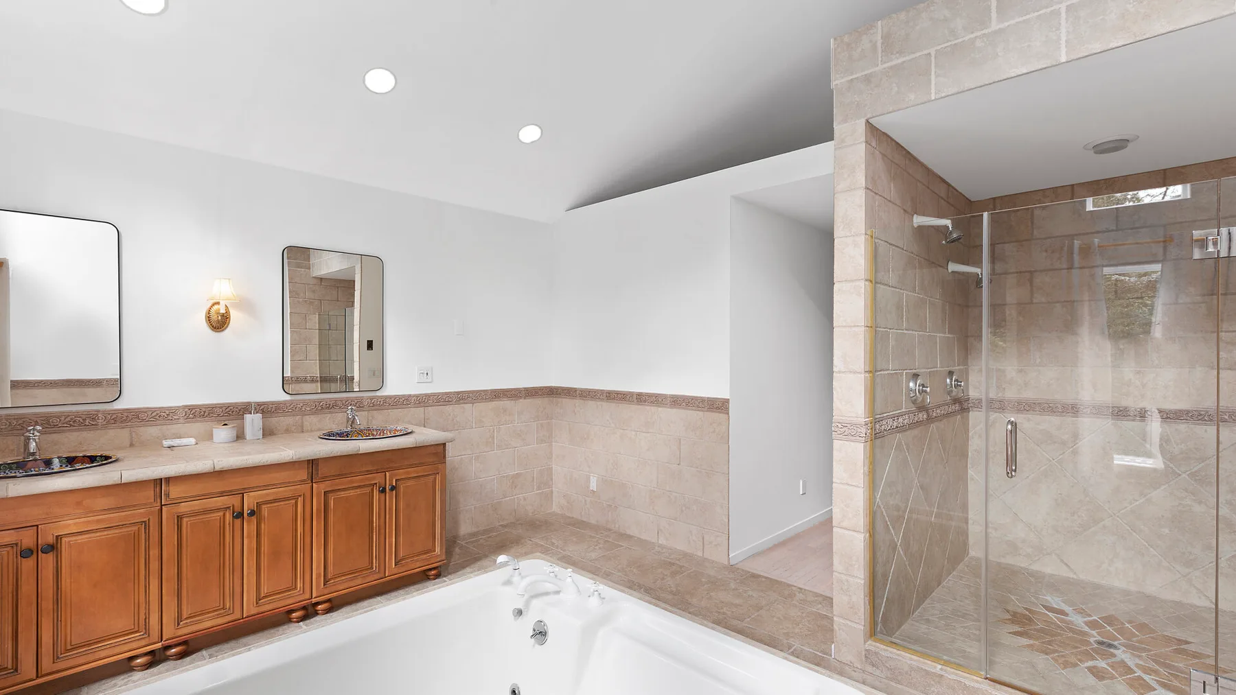 Un baño amplio con tocador de madera, bañera y ducha con mampara de vidrio.