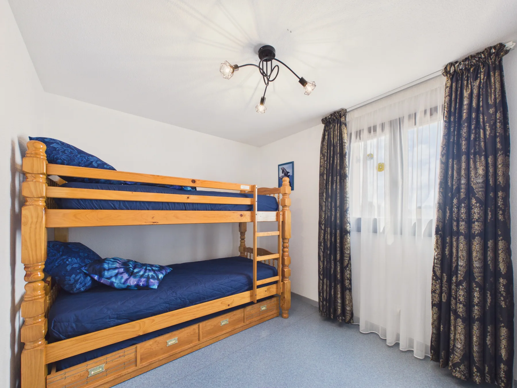 A bedroom with a wooden bunk bed and dark blue bedding.