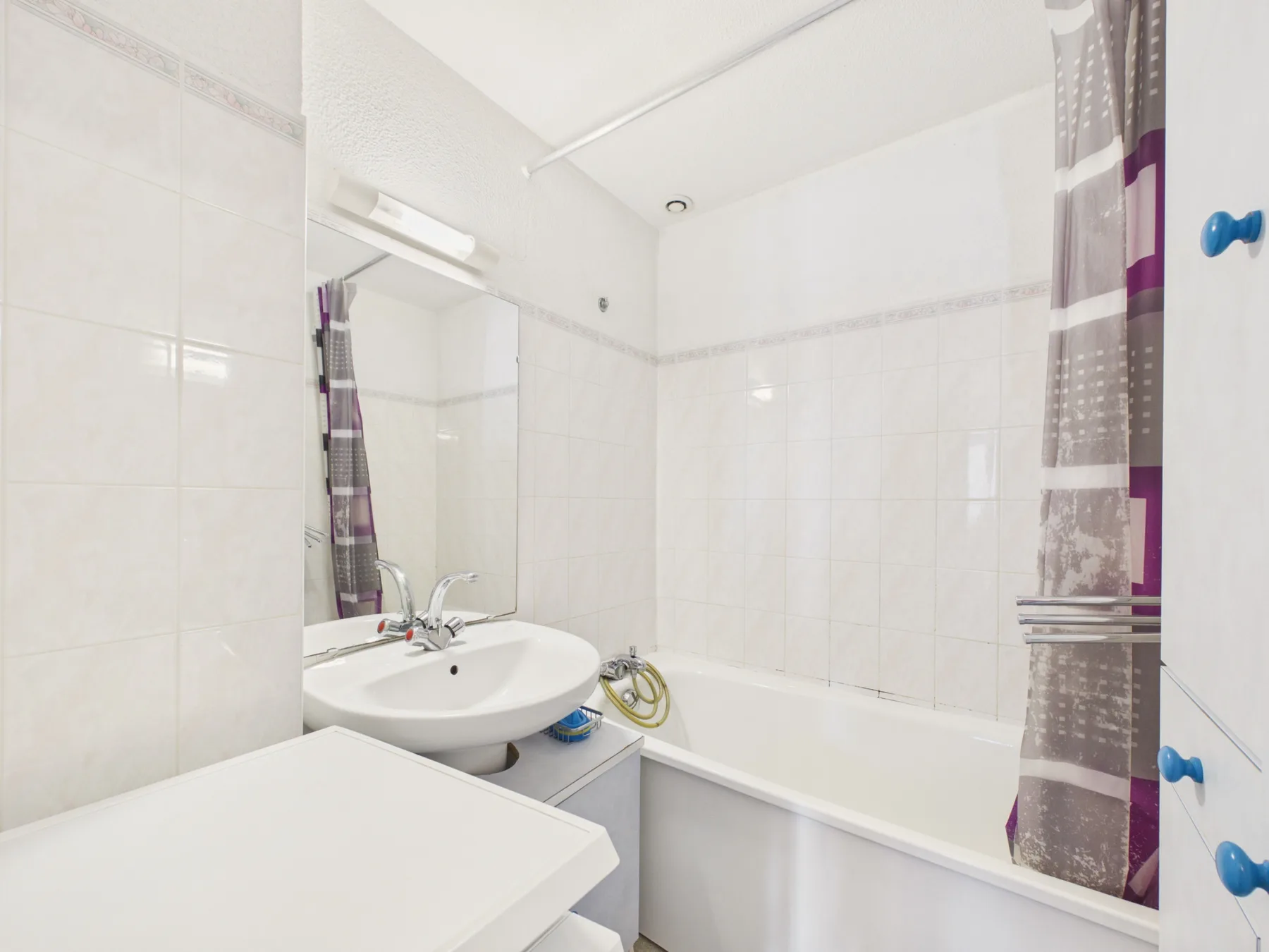 A tiled bathroom with a bathtub, sink, and patterned shower curtain.